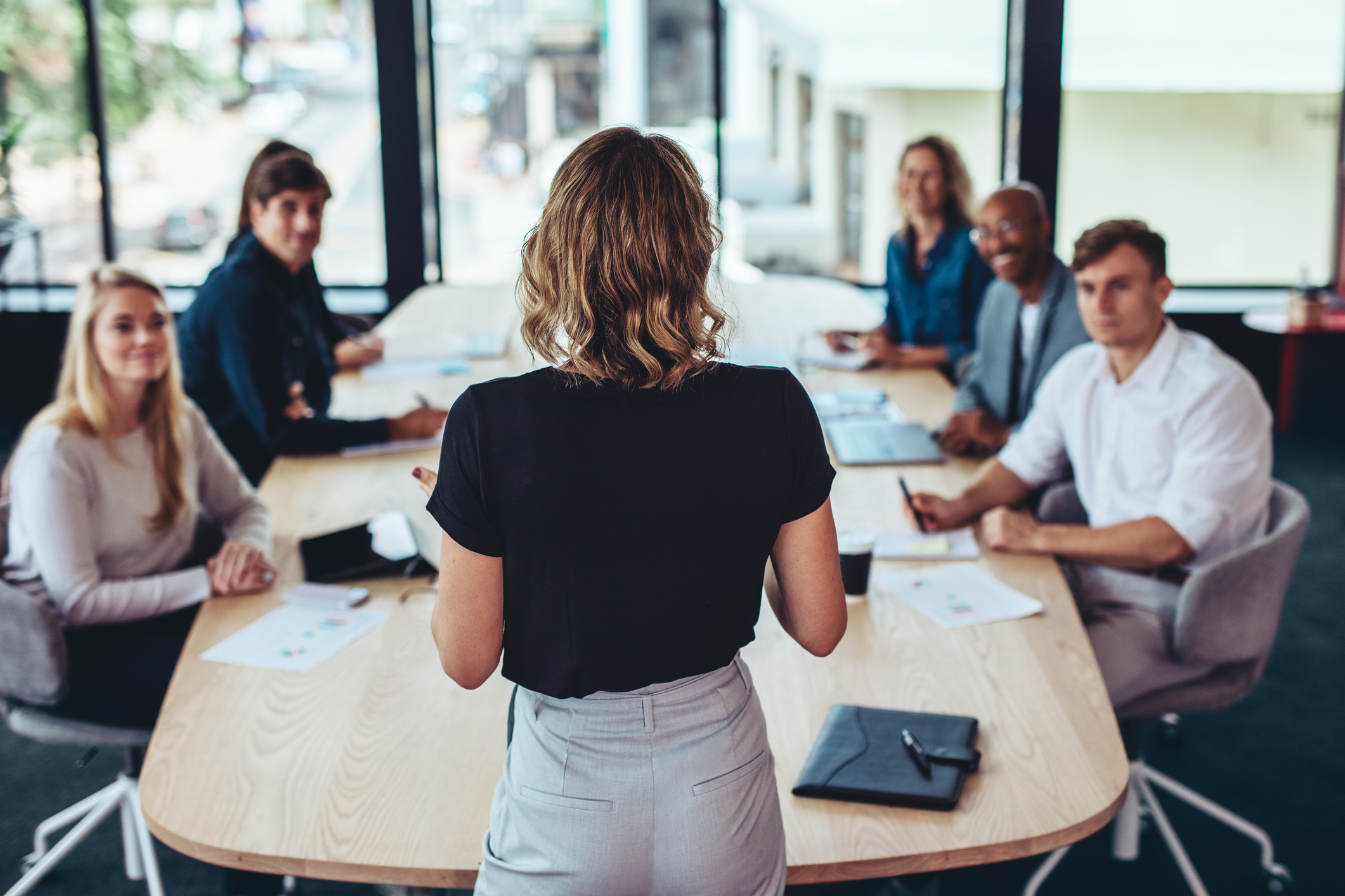 Business woman giving presentation on team meetings management to people sitting at conference table.
