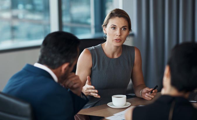 A female executive sitting with other business people in a meeting communicating her message.