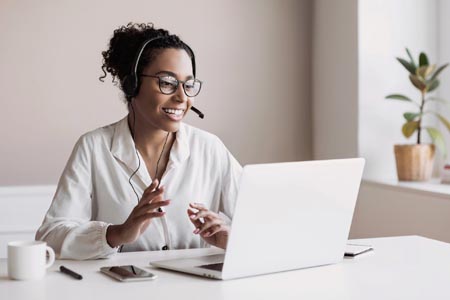 A woman wearing a headset and working on a laptop in an office helping customers with questions.