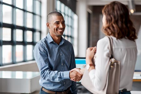 A male manager smiling while shaking a female employees hand after resolving a conflict in the office.