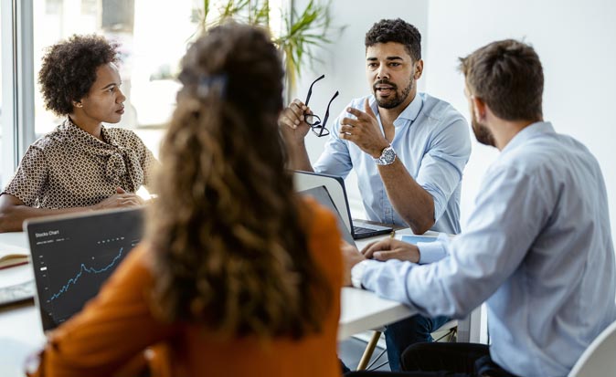 A group of people sitting around a table in an office with tense looks as they discuss a conflict.