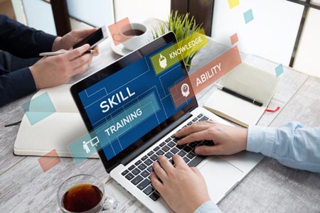 A business person typing on a laptop with the words skill training and ability shown on the screen.