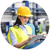 Female warehouse supervisor wearing a hardhat and holding clipboard and writing performance notes.