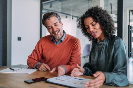 Two business people sitting at an office desk looking at a stack of team building reports.