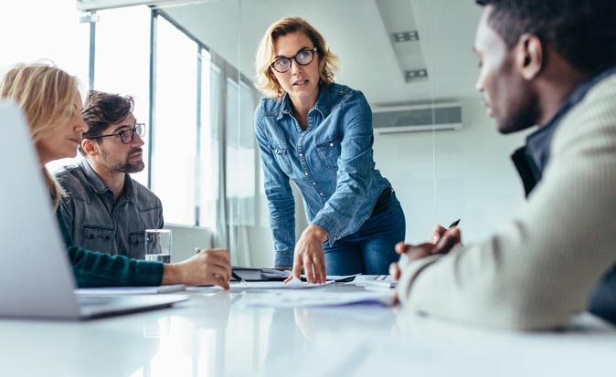 An instructor guides a group of managers sitting around a table learning new skills.