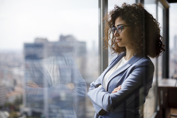 Young businesswoman standing in office looking outside through window.
