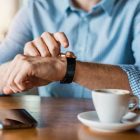 A man is sitting at a table with a cup of coffee and a smart watch.